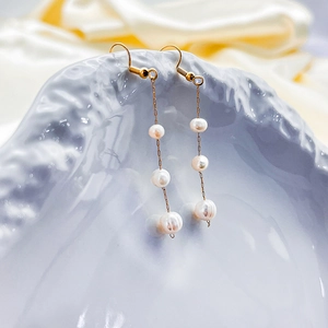 Détail de boucles d'oreilles pendantes en perles baroques dorées avec chaîne sur fond soie