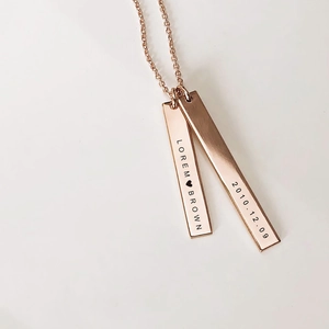 Macro shot of custom engraved rose gold rectangular bar pendants on a delicate chain