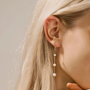 Boucles d'oreilles pendantes dorées avec trois perles blanches graduées sur un modèle