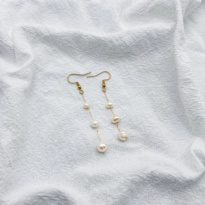 Détail de boucles d'oreilles dorées avec perles de culture baroques sur chaînes fines