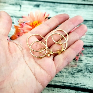 Detailed view of gold hoop earrings with hanging chain and bead details held by hand