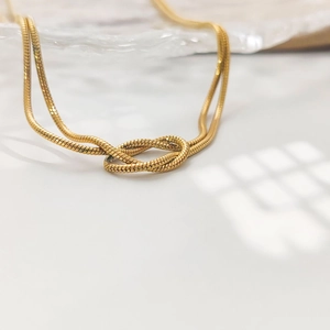 Vue macro d'un collier chaîne serpent dorée avec un nœud central sur plateau en verre