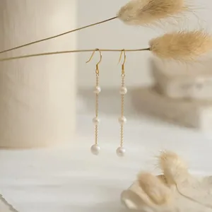 Détail de boucles d'oreilles dorées avec trois perles d'eau douce baroques blanches