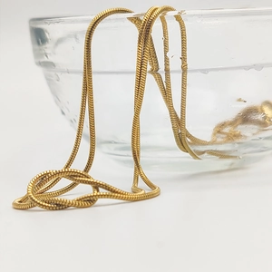 Vue détaillée du collier maille serpent doré étanche sur le bord d'un bol en verre