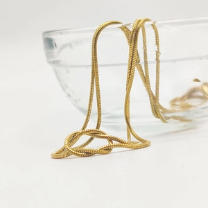 Élégant collier chaîne serpent en acier titane doré posé sur un bol en verre