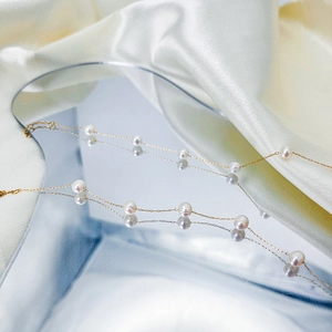 Minimalist gold chain pearl necklace with white pearls on a mirror and silk background
