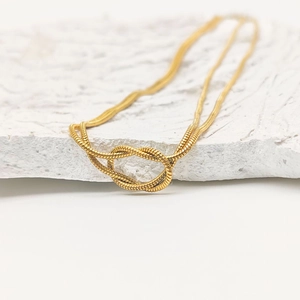 Détail d'un collier chaîne serpent dorée nouée avec un design à double maillon texturé
