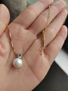 Close-up of gold box chain necklace featuring a white pearl and sparkling zircon pendant