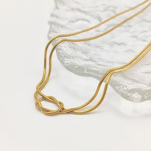 Gros plan d'un collier chaîne serpent en acier doré avec nœud sur plateau en verre