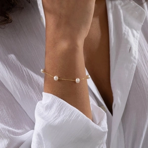 Detailed close-up of a minimalist gold pearl bracelet on a white textured fabric background