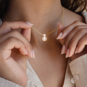 Detail of elegant pearl and zircon pendant on a gold box chain worn by a model
