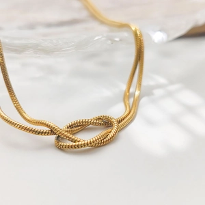 Détail d'un collier chaîne serpent dorée avec un nœud élégant en acier inoxydable
