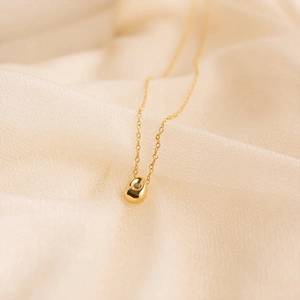 Close-up of a gold teardrop pendant necklace with a clear zircon on beige fabric