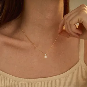 Detail of elegant gold chain necklace featuring a white pearl and zircon pendant on a model
