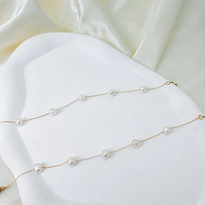 Macro shot of minimalist golden chain bracelet with scattered white baroque pearls