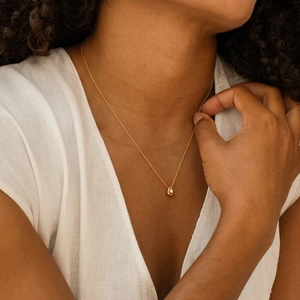 Close-up of minimalist gold teardrop pendant necklace with zircon on model's neckline
