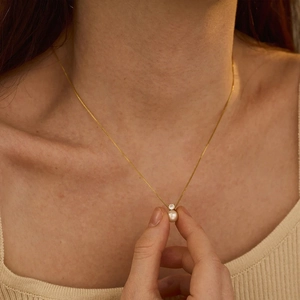 Close-up of a pearl and zircon pendant necklace on a gold chain worn by a model