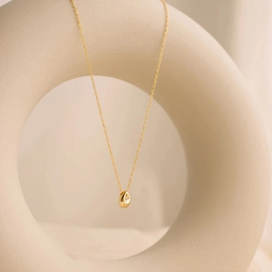 Detailed view of teardrop crystal pendant on gold chain against ceramic backdrop