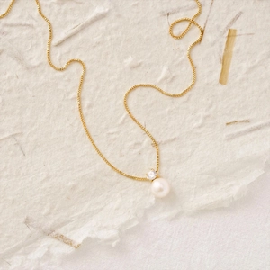 Detail of elegant gold-plated box chain necklace with white pearl and zircon pendant