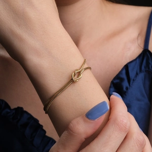 Macro detail of gold-plated knot snake chain bracelet on model's wrist with velvet background
