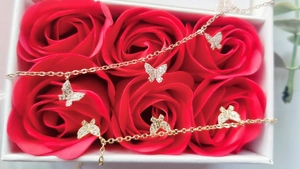 Détail d'un bracelet papillon doré avec oxydes de zirconium dans un coffret de roses rouges