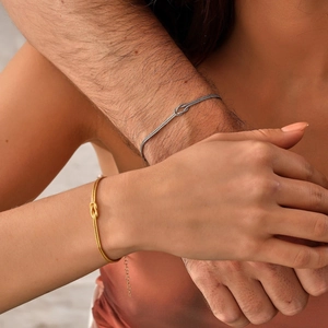 Close-up of gold and silver knotted snake chain bracelets worn by a couple