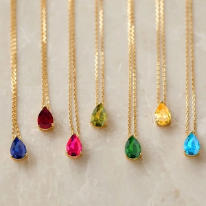 Détail de pendentifs en zircon colorés en forme de poire sur de fines chaînes dorées