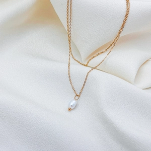 Gros plan d'un collier doré à deux couches avec un pendentif en perle blanche en forme de goutte