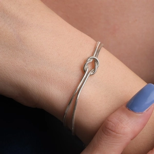 Detail shot of silver double-strand snake chain bracelet featuring a central love knot
