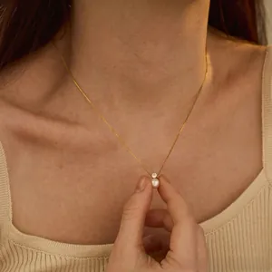 Close-up of minimalist gold necklace featuring a white pearl and zircon pendant on a model