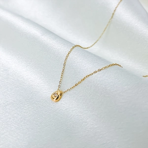 Detailed shot of a gold teardrop pendant necklace with zircon on white satin fabric
