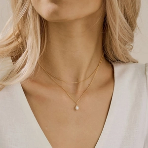 Détail d'un collier double rang doré avec un délicat pendentif perle blanche sur mannequin