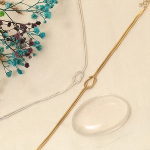 Minimalist gold and silver snake chain knot bracelets displayed on neutral fabric background