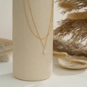 Collier double couche doré avec pendentif perle baroque blanche sur support épuré