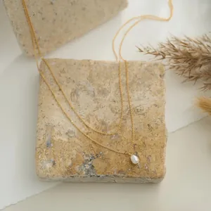 Détail d'un collier à double chaîne dorée avec une perle goutte blanche sur pierre
