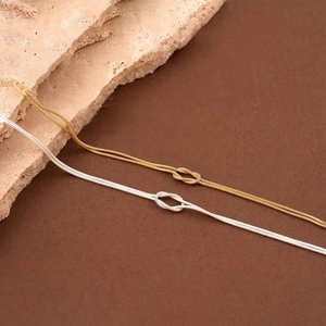 Macro shot of minimalist gold and silver knot snake chain bracelets on textured stone