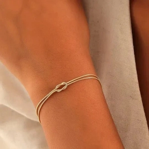 Close-up of a minimalist gold-plated knot bracelet on a model's wrist against fabric