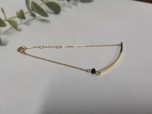 Detail of golden stainless steel bar bracelet with black bead and lobster clasp