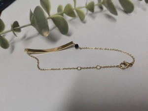 Detail of gold bar bracelet with a single black bead on a white minimalist background