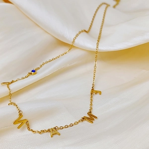 Detalle de collar dorado con letras WAME y piedra de nacimiento azul sobre satén