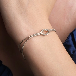 Detail of silver double-strand snake chain bracelet featuring a central knot design on wrist