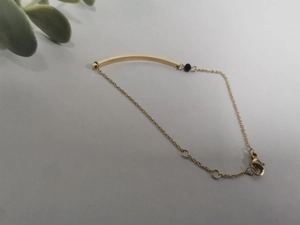 Detailed view of gold stainless steel bar bracelet with small black bead and lobster clasp