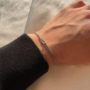 Close-up of a silver knot snake chain bracelet worn on a wrist showing metallic shine