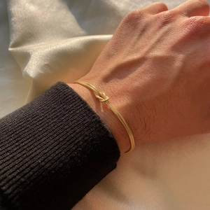 Detail of a minimalist gold knot snake chain bracelet worn on a female wrist over silk