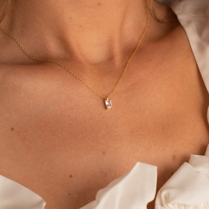 Close-up of golden necklace with emerald-cut zircon pendant on model neck