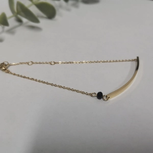 Minimalist gold titanium steel bracelet with a curved bar and black bead accent