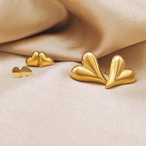 Détail de trois paires de boucles d'oreilles cœur dorées sur un élégant satin champagne