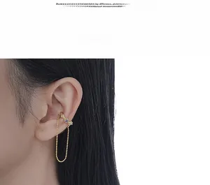 Détail d'un ear cuff doré avec pierres de zircon violettes et longue chaîne perlée