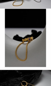Détail d'une bague dorée texturée avec pierre précieuse violette et chaîne perlée