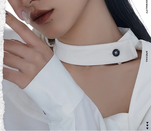 Détail du décolleté asymétrique et de la bride boutonnée sur une chemise blanche